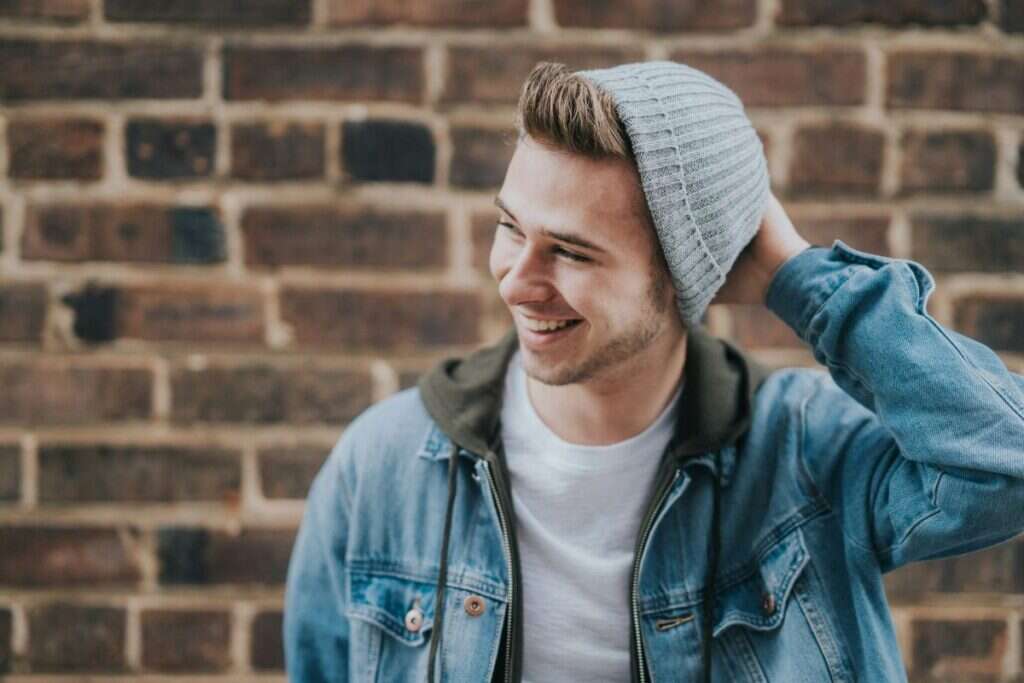 Junger Mann mit Mütze vor eine Klinkerwand. Lacht und schaut nach links.&nbsp;– Foto: Jeremy McKnight via Unsplash